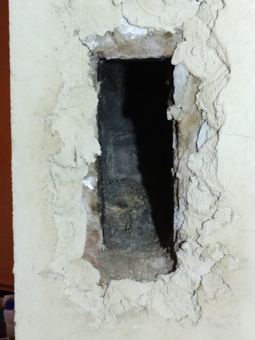 Fyrkantigt hål i en vägg för anslutning till skorsten, omgiven av putsat material.