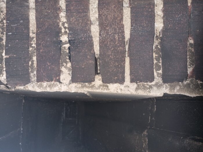 Närbild av tegelfog på en skorsten med mörkt tegel och sliten murbruk, fokus på fogens struktur och kvalitet.