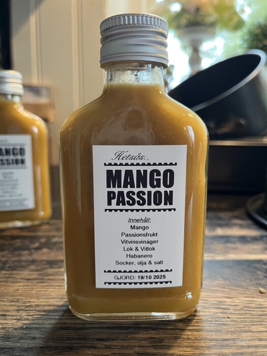 Flaska med hemmagjord hetsås, etikett "Mango Passion", innehåller mango, passionsfrukt, habanero. Gjord 19/10 2025.