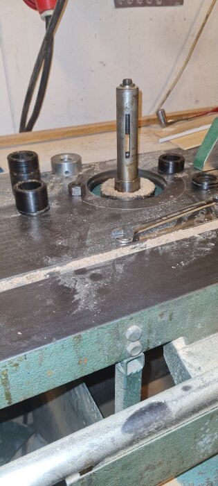 Gammal maskin med synlig spindel och gängstång på verkstadsbord, omgiven av verktyg och sågspån.