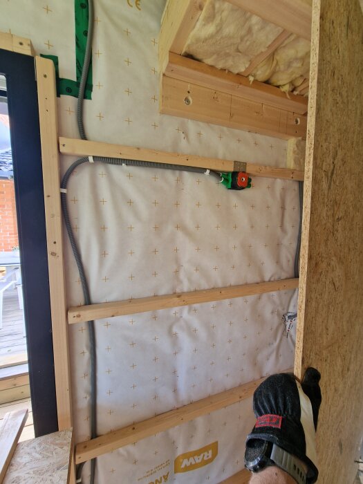 Installation av eldragning och isolering på vägg, med synlig träkonstruktion och OSB-skiva under montering.