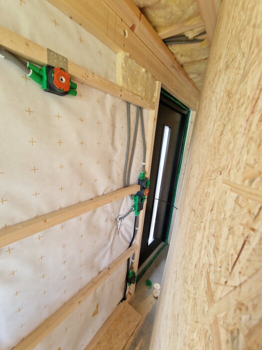 Elektrisk installation i pågående byggprojekt med elledningar, träreglar och isolering, samt OSB-skiva på väggen.