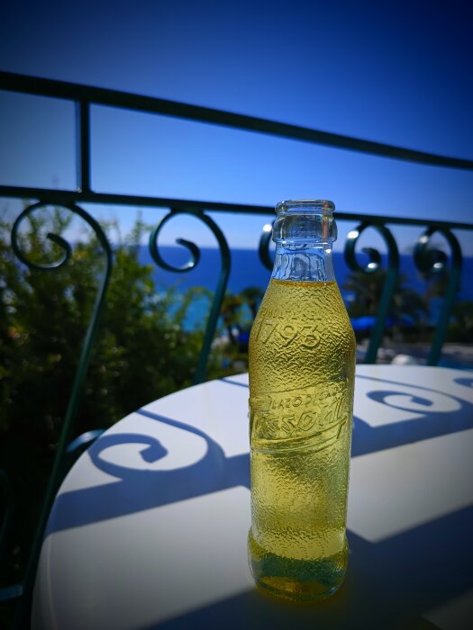 Flaska med Cedrata på ett bord utomhus, med blå himmel och hav i bakgrunden.