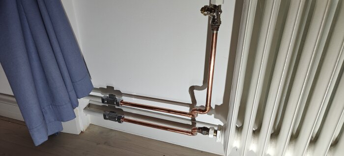 Kopparrör som ansluter till element bredvid en blå gardin.