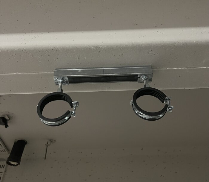 Två svarta och silverfärgade rörfästen monterade i taket, fästa på en metallstång i ett garage.