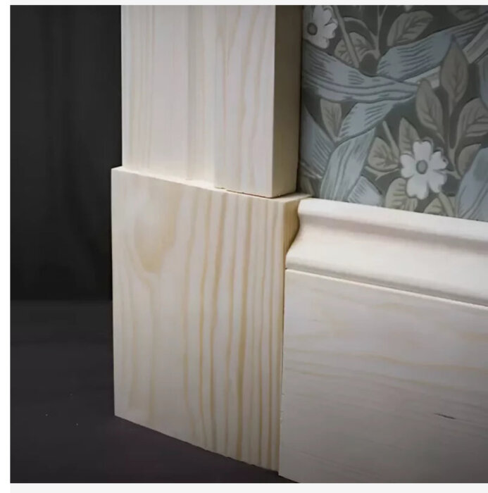 Närbild av träfoder med sockelkloss monterad vid tapetserad vägg.