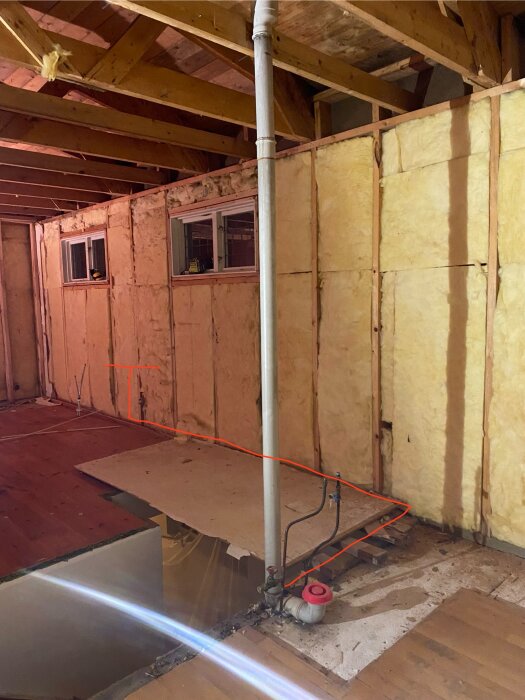 Byggprojekt med isolerade väggar, synliga rör och ett rött streck markerande framtida avloppsdragning bakom väggen.