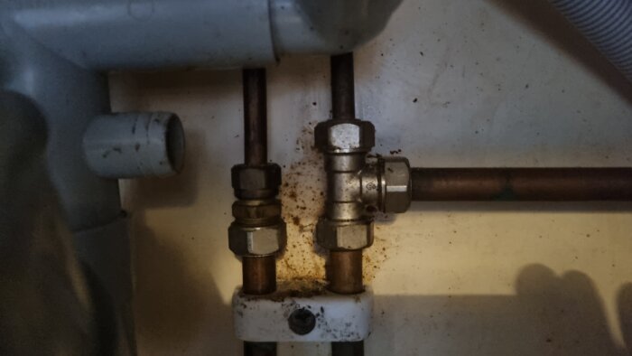 Kopplingar under en diskbänk med rost och smuts, olika storlek på muttrarna på varm- och kallvattenanslutningar.