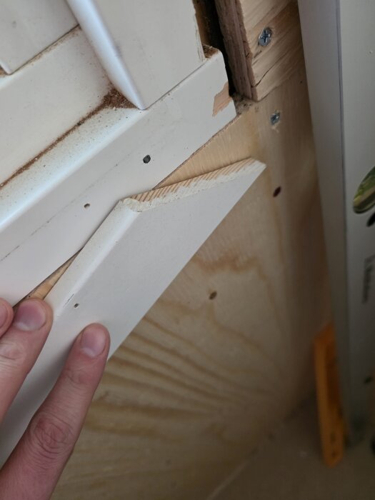 En person tar bort en list från ett fönster för att förbereda för montering av tätskikt på en byggskiva.