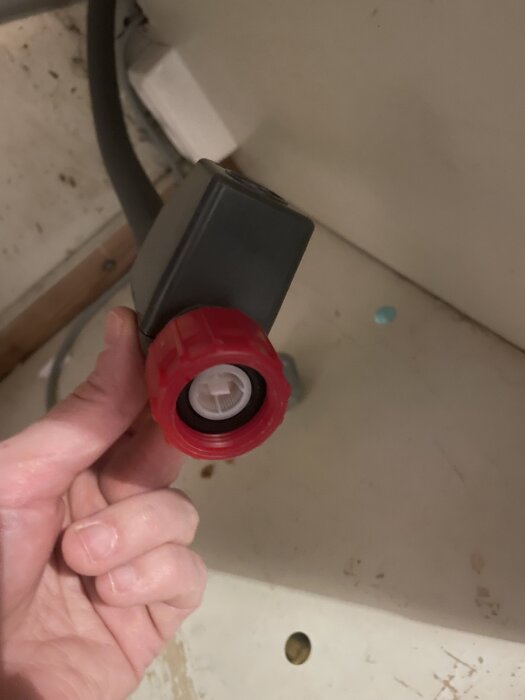 Röd bussning och grå anslutning del av diskmaskinkoppling, hålls i en hand.