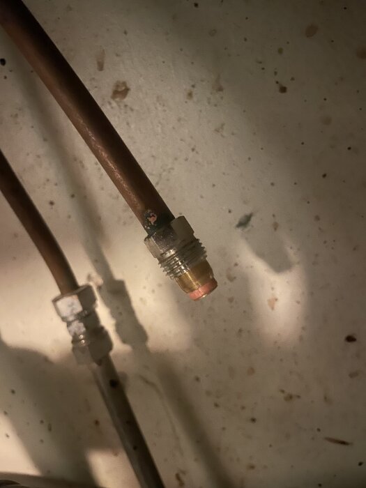 Gängad vattenkoppling under en diskbänk med metallrör i närbild. Kopplingen är ansluten till en vattenledning.