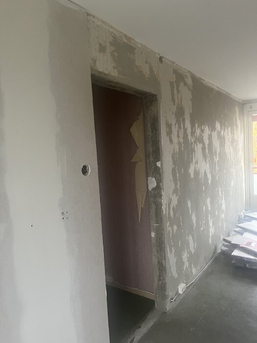 Orenoverad vägg med igenbyggd dörröppning där gipsskivor och spackel har använts; gamla tapetrester synliga på resten av väggen.