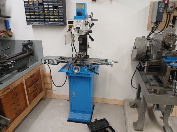 Arbetsplats i garage med ny borr- och fräsmaskin, omgiven av verktyg och arbetsbänkar.