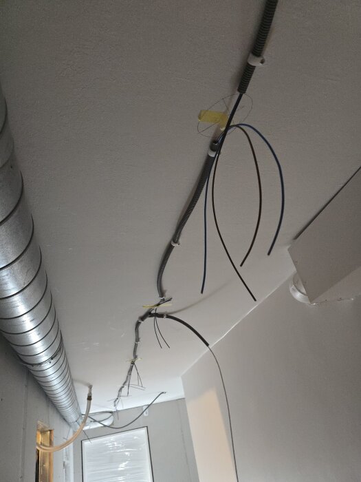 Tak med installationsrör och kablar för belysning, omgivande ventilationselement, vilket indikerar en pågående renovering.