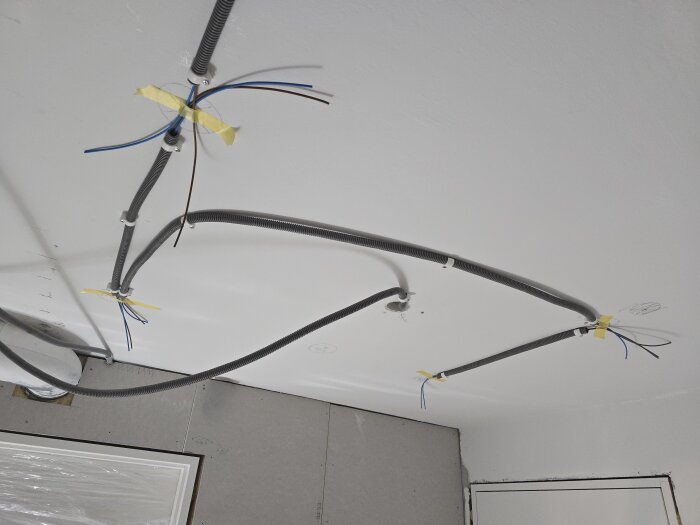 Elektriska flexrör monterade i ett tak, förberett för installation av takspottar. Kablar hänger ut på flera ställen, fasttejpade med gul tejp.