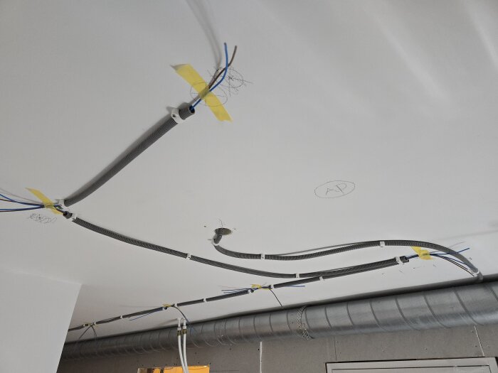 Elektriska flexrör och sladdar är fasttejpade längs taket under installation till takspottar i ett renoveringsprojekt.