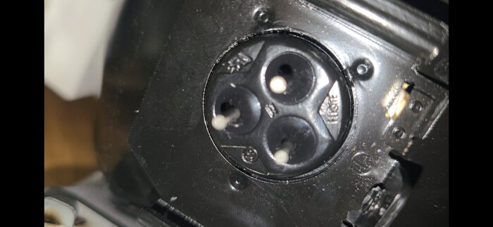 Närbild av ett svart runt kontaktuttag på en kompressor med tre stift och märkningar runtom.