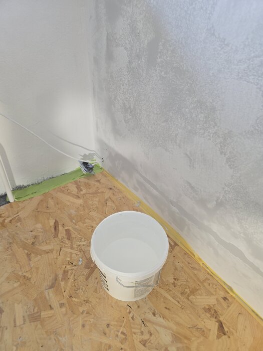 Spacklad vägg med osb-golv, maskeringstejp vid golvlist och plastspann vid renovering.