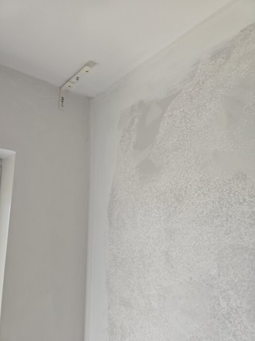 Vägg med grundfärg och fläckar av spackling, tydligt hörn och takfäste synliga.