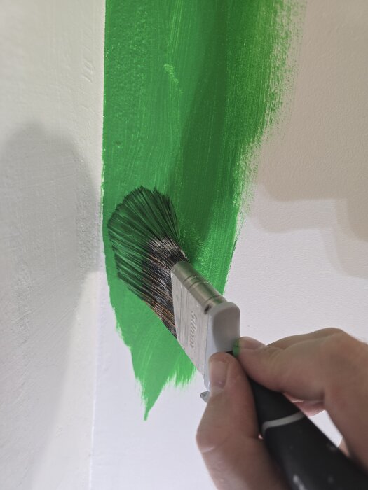 Målning av en vägg med grön färg med en pensel, del av ett barnrumsrenoveringsprojekt.