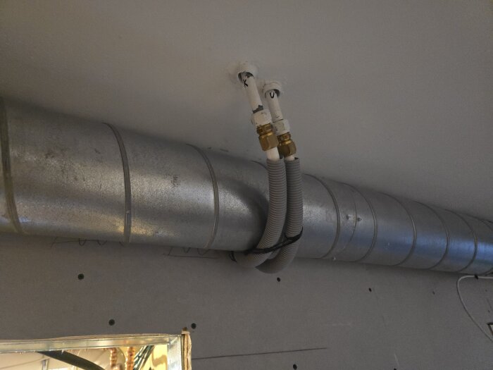 Metallrör och grå flexrör syns monterade i ett tak ovanför en öppning, förberedelser inför renovering.