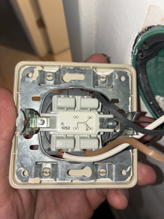 Väggmonterad brytare med svarta och bruna kablar synliga, inre komponenter och kopplingsschema på ett vitt plasthölje.