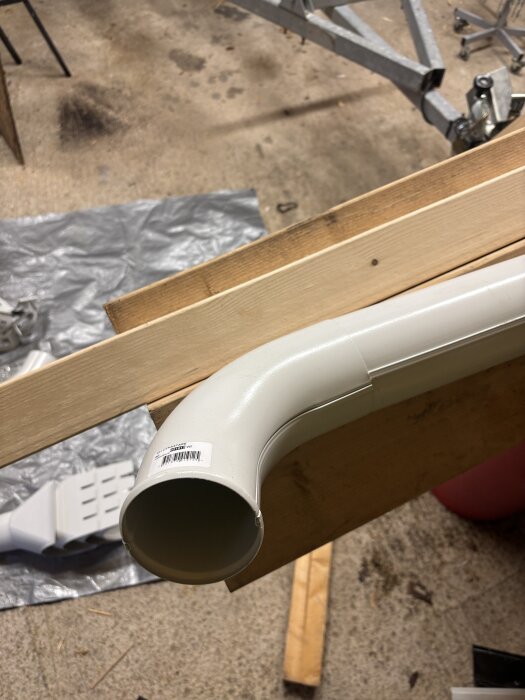 Vit plastböj med skarvdel ligger på träplankor i en verkstad.