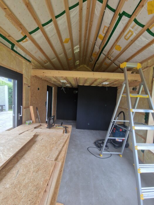 Renoveringsprojekt: isolerat rum klart för toalett, köket ska byggas. Visar stege, verktyg och väggar med isolering.