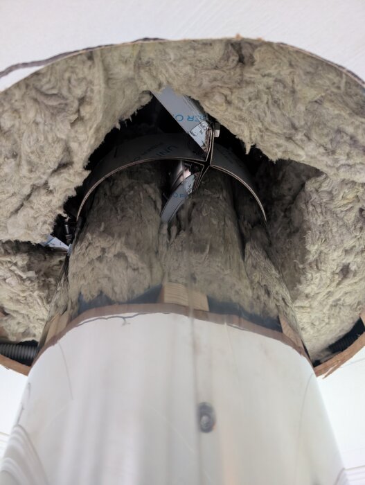 Rökkanal omgiven av stenull i taket, diskussion om isoleringens värmetålighet för att minska kallras.