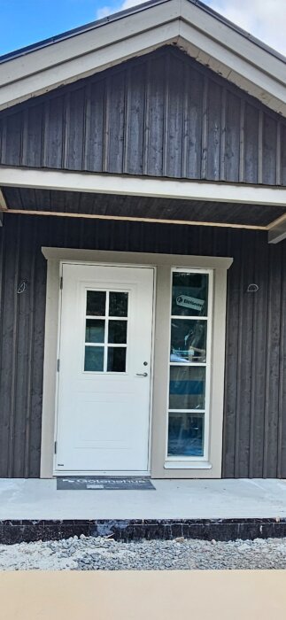 Entré med vit dörr och fönster, träram och saknade ytterlampor. Planerad montering innan slutbesiktning.