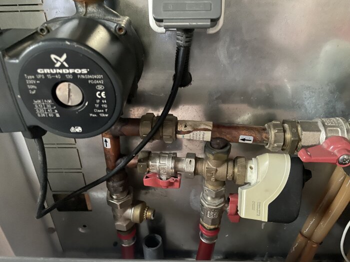 LK golvvärmesystem med strypventil och pumpar, märkt Grundfos, i ett tekniskt utrymme för fjärrvärmejustering.