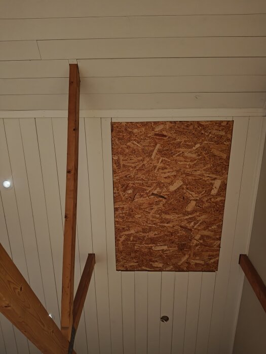 Rektangulärt område i tak med plywood istället för panel, omgiven av träreglar.