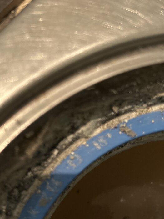 Golvbrunn i dusch med blå ring, delvis borttagen silikon och trådliknande material synligt. Fokus på kant och material inblandade i brunnen.