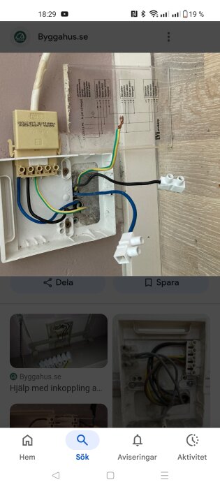 Öppnad väggdosa med synliga elektriska kablar, en gul och grön jordkabel samt blå och svarta strömkablar. Elektrisk installation pågår.