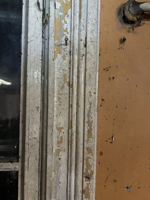 Gammalt fönsterfoder med avskavd färg och sliten yta, placerat mot en orange vägg.