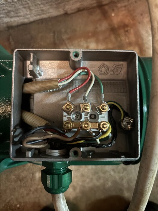 Närbild av anslutningarna i en grön jetpump, flera färgade kablar är inkopplade i en metallplint inuti pumpen.