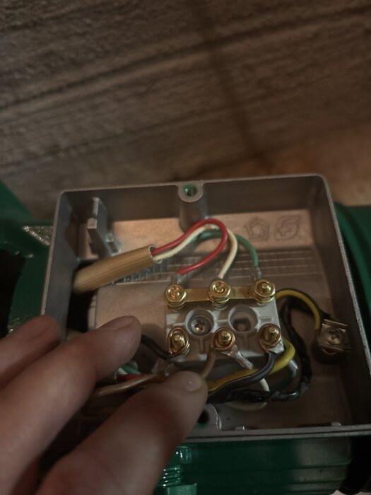 Elektrisk kopplingsdosa med flera färgade kablar anslutna till klämmor och en hand som håller några av kablarna.