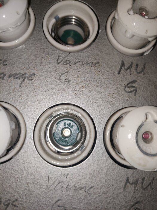 Keramiska säkringar märkta 6A och 400V med handskriven text "Värme" och "MU" på en grå panel.