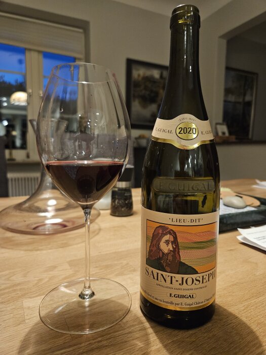 Flaska Saint-Joseph vin från 2020 med vinglas bredvid, på ett träbord i hemmiljö.