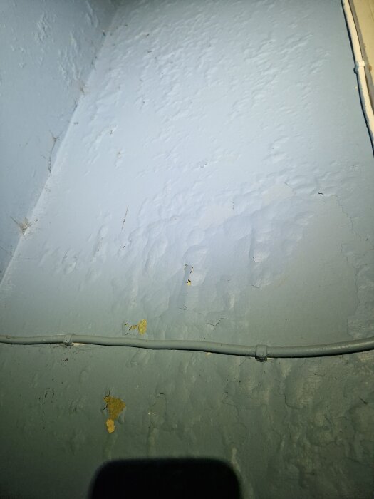 Vägg med blå färg och synliga blåsor samt flagning. En kabel löper längs väggen som har textur och tecken på renoveringsarbete.