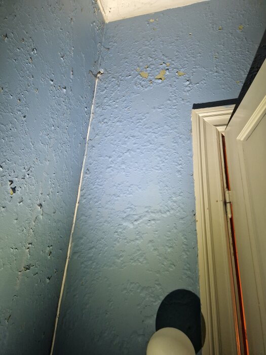 Blå vägg i hall med flagnande färg och ojämn textur nära hörn, del av renoveringssituation i gammal skola från 1800-talet.