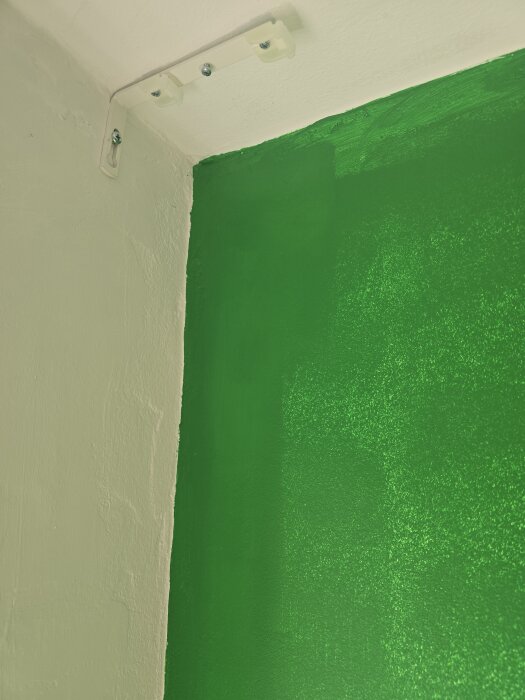 Grönt och beige hörn av ett rum med tydlig färggräns, synligt fäste på väggen.