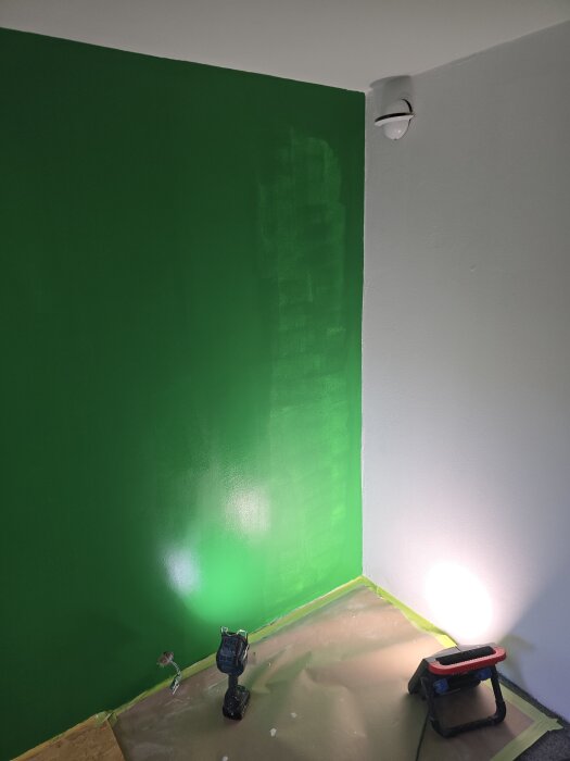 Ett rum med nymålade gröna och vita väggar, en lampa och verktyg på golvet för belysning och arbete.