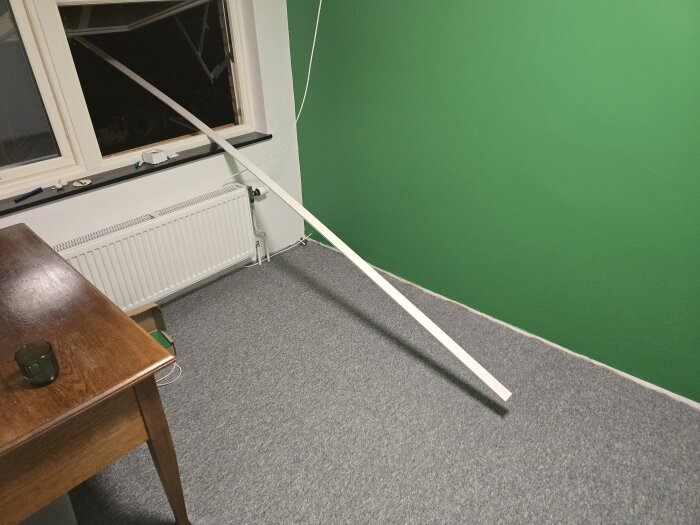 Grönt nymålat rum med en golvlist placerad diagonalt över golvet. En öppetstående fönster, ett element och ett träbord syns.