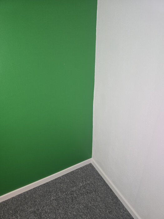 Gröna och vita väggar möts i ett hörn med grått golv och vita lister.