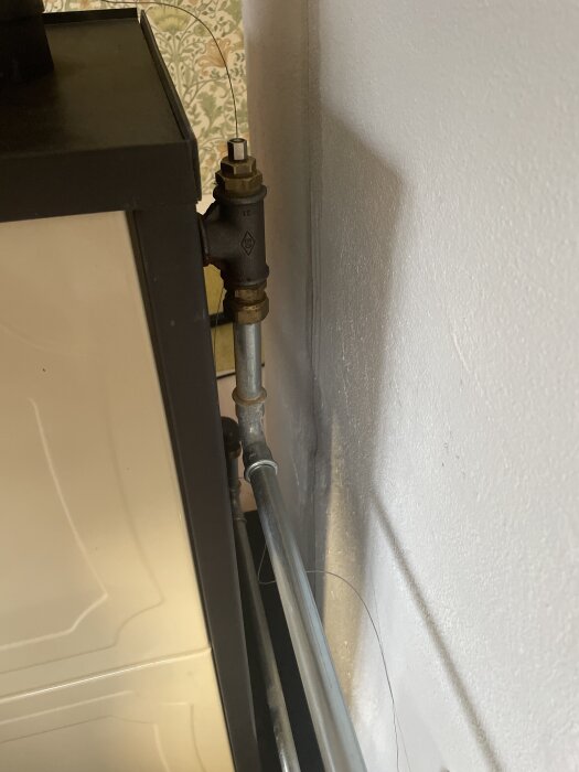 Ventil och rör bakom kökspanna, kopplade till värmesystem. Ventilen kan behöva bytas till en automatisk avluftare för att lösa luftproblem.