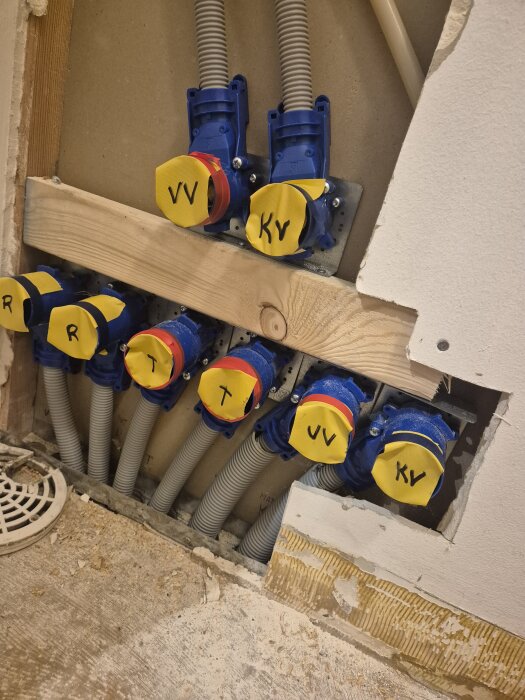 Bilden visar rörinstallationer med märkningar i ett vägguttag, med träbräda och synliga gipsskivor. Rören är märkta med "VV" och "KV".