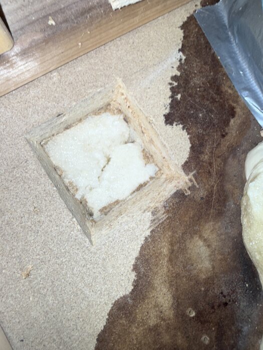 Uthugget rektangulärt område i spånskiva med synlig vit cellplastisolering under.