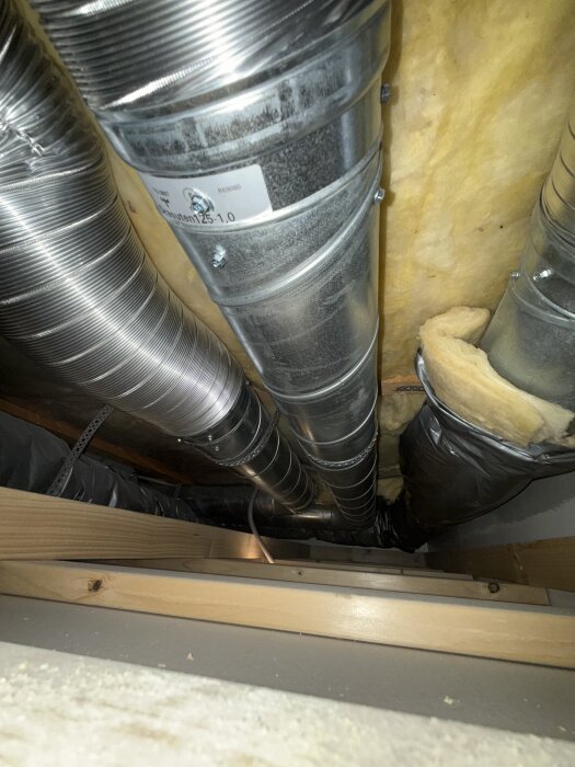 Runda ventilationsrör av metall under ett tak, med isolering synlig runt omkring.