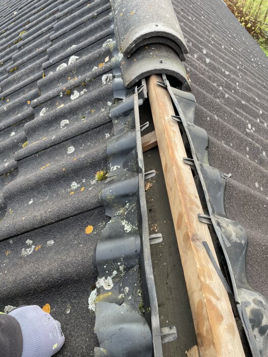 Tak med delvis exponerad nockpanna och sliten plast under. Tydlig glipa på vänster sida där takpannorna inte täcks korrekt.